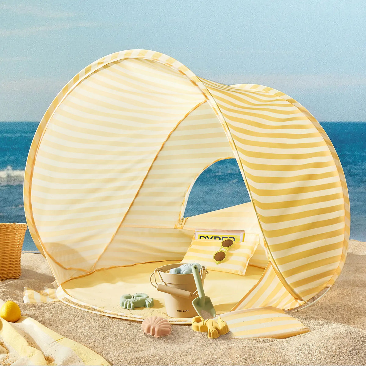 Kids Beach Tent & Sand Toy Set in pastel yellow stripes, set up on sand with a bucket, shovel, and molds inside.