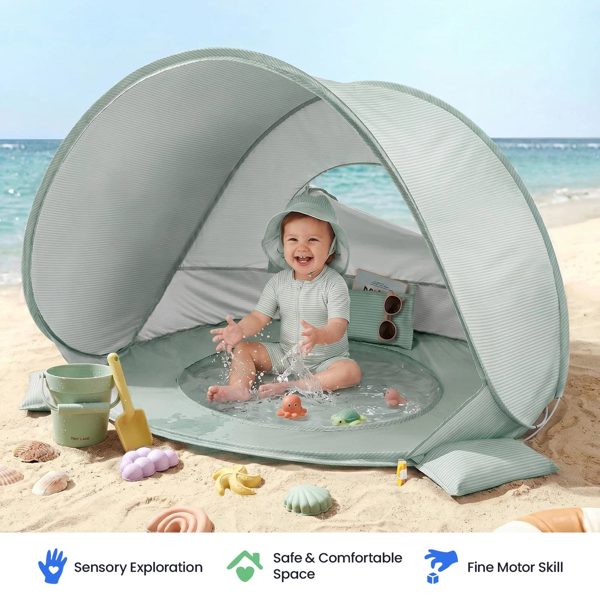 A baby sits in the built-in splash pool of a 3-in-1 Baby Beach Tent with Splash Pool, surrounded by various small plastic toys on the sand.