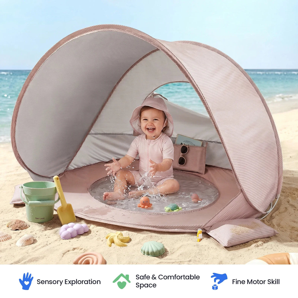 A baby sits in a 3-in-1 Baby Beach Tent with Splash Pool, surrounded by assorted plastic toys on the sand.