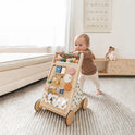 A baby pushes the Tiny Land® Versatile Natural Wooden Baby Walker on a striped rug in a cozy, sunlit living room, promoting sensory development with toys and decor visible in the background.