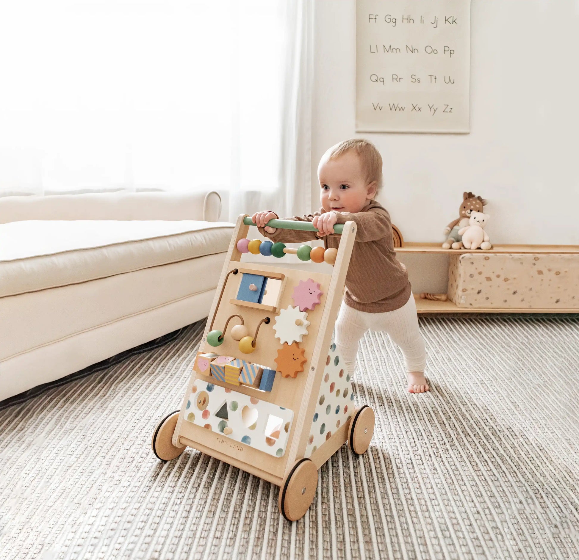 A baby pushes the Tiny Land® Versatile Natural Wooden Baby Walker on a striped rug in a cozy, sunlit living room, promoting sensory development with toys and decor visible in the background.