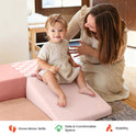 A toddler sits on a pink PlayNest Soft Foam Climbing Blocks – Violet ramp, part of a soft play furniture set, as a woman sits beside her.
