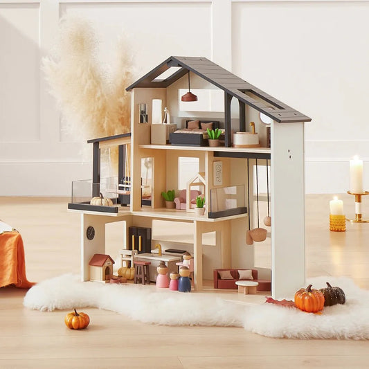 The Tiny Land® Sweetwood Edge Dollhouse, featuring multiple rooms, miniature furniture, and decor, sits on a fluffy white rug. Fall accents—like small pumpkins—and candles add a cozy touch nearby.