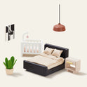 Create a modern, minimalist bedroom in the Tiny Land® Sweetwood Edge Dollhouse with a black bed, beige bedding, white crib, beige nightstand, green potted plant, modern wall art, and a brown hanging lamp on a light backdrop.
