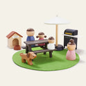 Create a charming picnic scene for your Tiny Land® Sweetwood Edge Dollhouse with four wooden figures, a dog, picnic table, grill, doghouse, white umbrella, and accessories—all on a circular green felt mat.