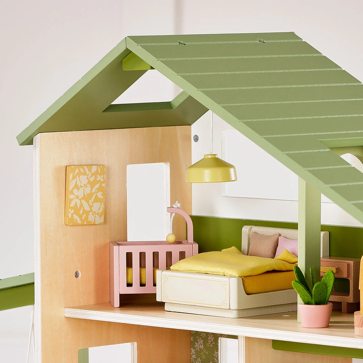 A 1:12 scale Sweetwood Cottage Dollhouse bedroom featuring a bed, a crib, a hanging pendant lamp, and a small potted plant.