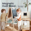 Two kids draw on the Tiny Land® Magnitales Easel for Kids - Green, featuring magnetic dual sides—a chalkboard and a whiteboard. The easel has a tray underneath and stands in a cozy room. Inset images show both blank surfaces. Text reads: Magnetic Dual Sides.