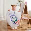 A toddler holds up a large sheet of paper with colorful abstract drawings in front of a Magnitales Double-Sided Art Easel with Paper Roll.