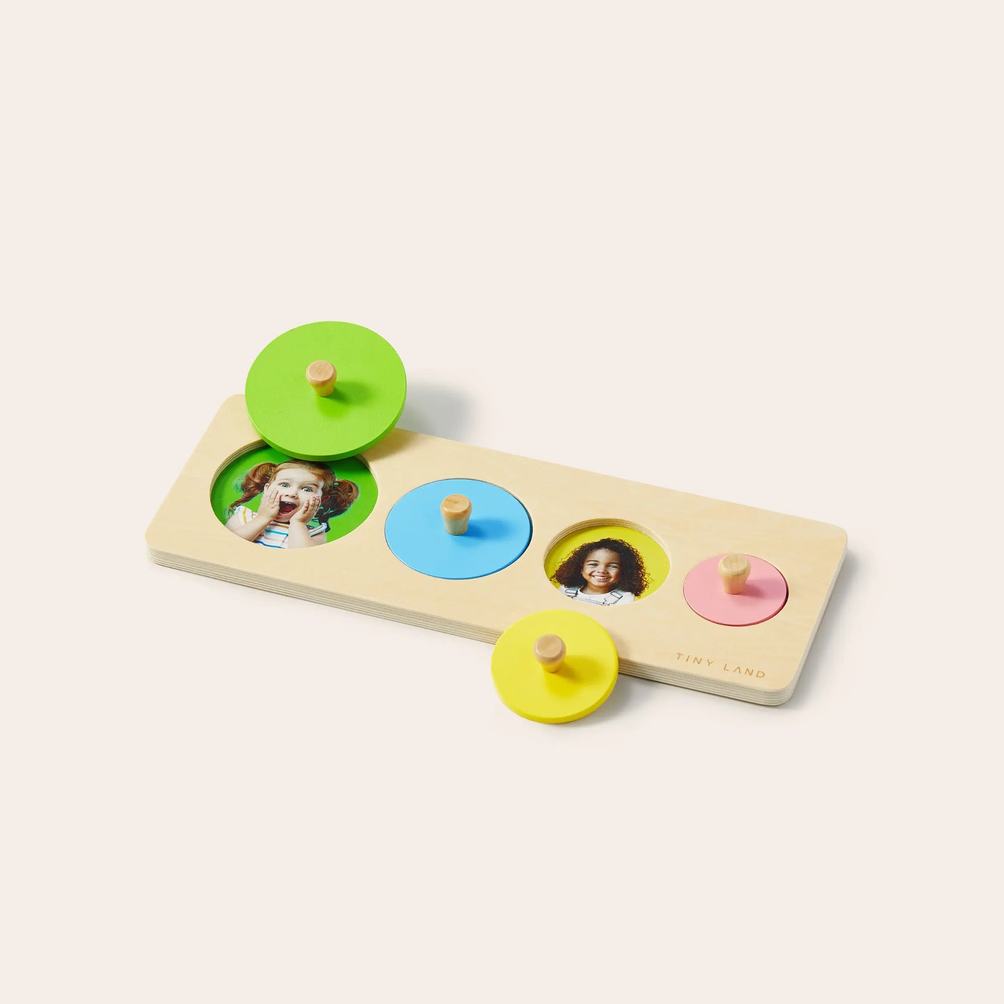 The Tiny Land® Montessori Toys for Toddlers (13–15 Months) features a wooden puzzle with green, yellow, and blue peg pieces. Two pieces are removed to reveal photos of smiling children underneath—perfect for early Montessori learning.