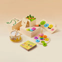 Tiny Land® Montessori Toys for Toddlers (13–15 Months) includes colorful wooden drum, stacking rings, carrots, shape sorters, and a Colors booklet—all arranged on a light beige surface. Ideal early learning box for little ones.
