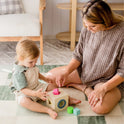 A toddler and an adult sit on a checkered mat, playing with the Tiny Land® Montessori Toys for Toddlers (16–18 Months), fitting colorful shapes into matching holes—an ideal educational toy for early learning.