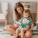 A woman reads to a 16–18 month old on her lap in a cozy room with a checkered rug. Nearby are Tiny Land® Montessori Toys for Toddlers (16–18 Months) – Montessori Educational Toys, along with other toddler learning items.