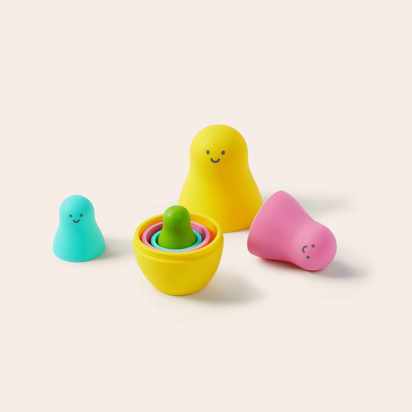 Four rounded, colorful figures with smiling faces, including aqua, yellow (with nested rings), and pink pieces—part of the Tiny Land® Montessori Toys for Toddlers (16–18 Months), an ideal educational set shown on a light background.