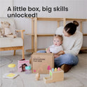 A woman sits on the floor with a baby next to a Tiny Land® Montessori Toys for Infants (10–12 Months) box filled with wooden toys and a book titled Emotions. Text above reads, "A little box, big skills unlocked!" in a cozy, light-filled room.