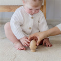 An infant sits on a light carpet while an adult helps them place a wooden egg from the Tiny Land® Montessori Toys for Infants (10–12 Months) set on its stand.