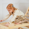 A child crawls on a 7-in-1 Montessori Climbing Set with Play Pad, featuring a flat, ramp-like surface with small block-like grips.