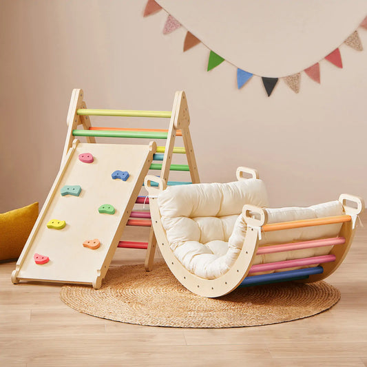 The 7-in-1 Montessori Climbing Set with Play Pad – Rainbow includes a wooden Pikler triangle with a slide and a cushioned rocking seat featuring colorful bars and a padded play cushion.
