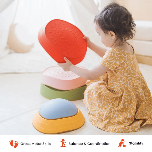 A child sits on the floor stacking colorful, rounded plastic Stacking Balance Stepping Stones – Vintage to create an obstacle course.