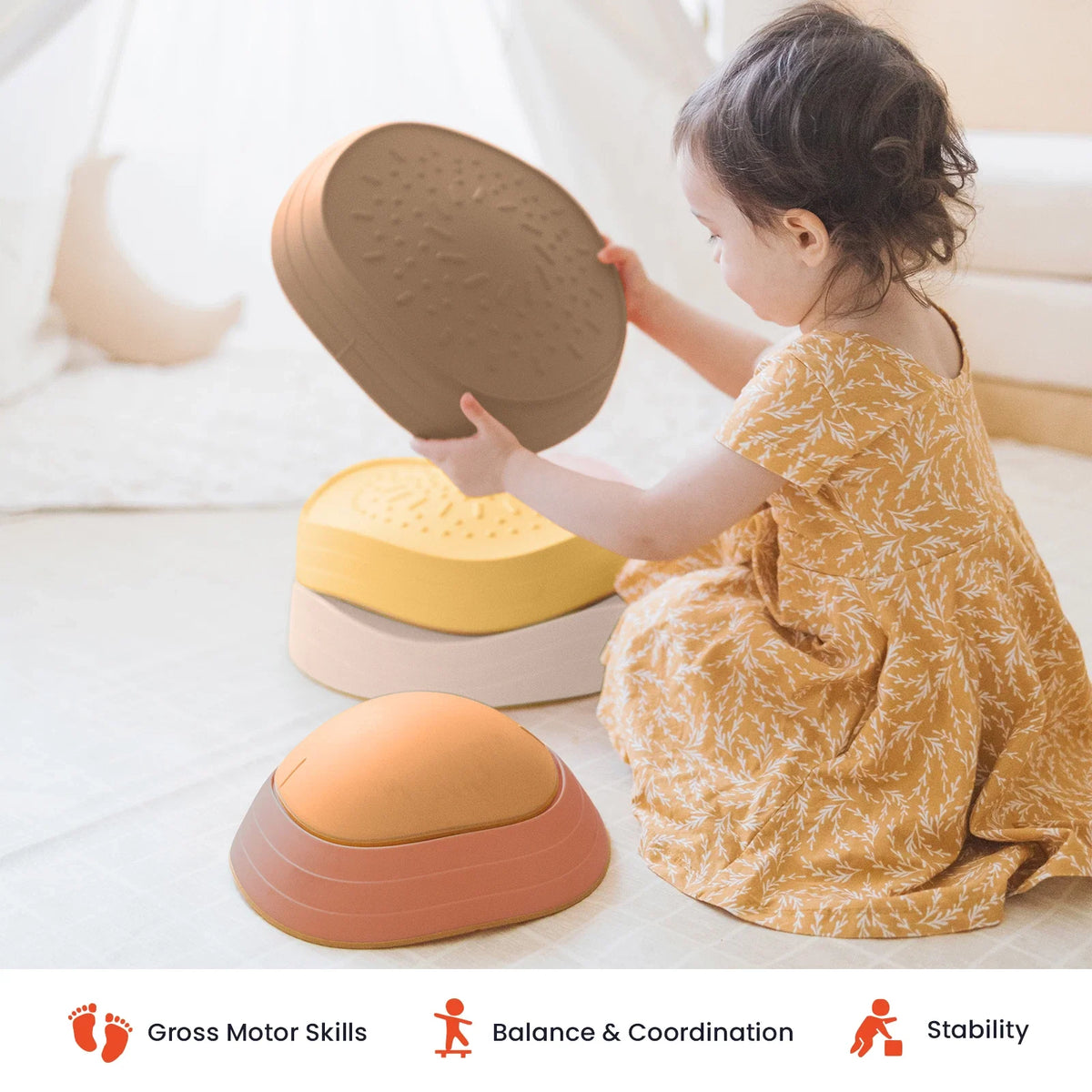 A young child stacks multicolored, dome-shaped Stacking Balance Stepping Stones – Sunset on a floor to create a balance course.