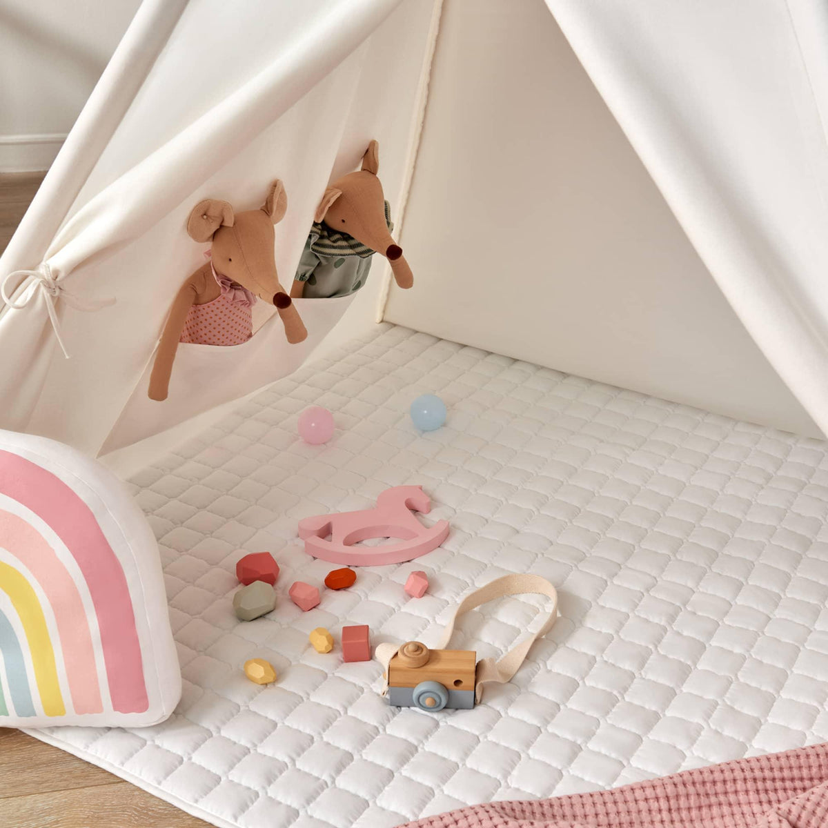 Cozy Kids Teepee Tent with Padded Mat featuring a white teepee, a padded floor mat, two stuffed mouse toys in a wall pocket, small wooden toys, and a rainbow-patterned bolster cushion.