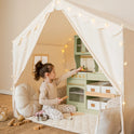 A child plays with a wooden toy kitchen inside a Large Cozy Cabin Play Tent with Star Lights decorated with string lights.