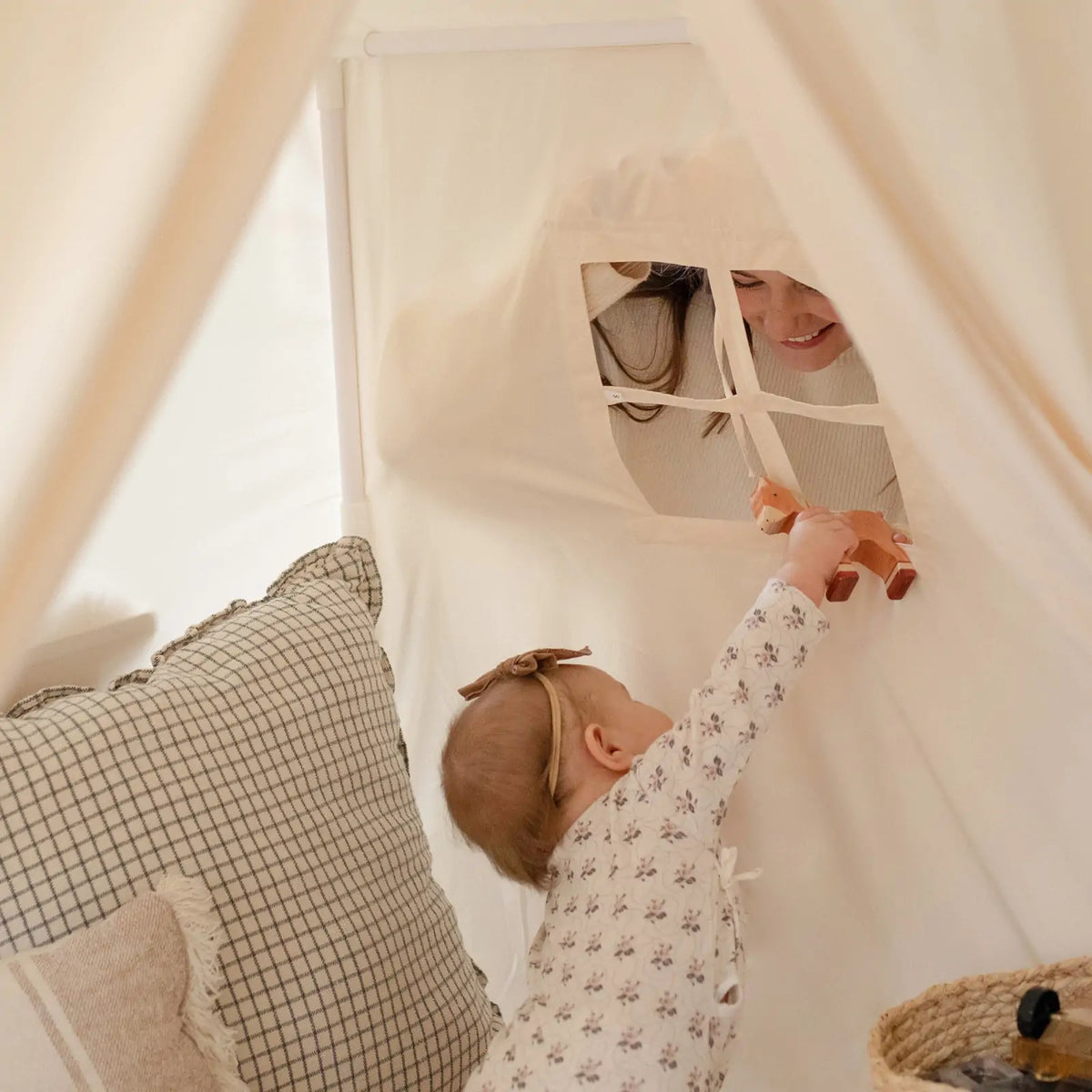 A baby reaches through a window in a Large Cozy Cabin Play Tent with Star Lights to hand a wooden fox toy to an adult peering in.