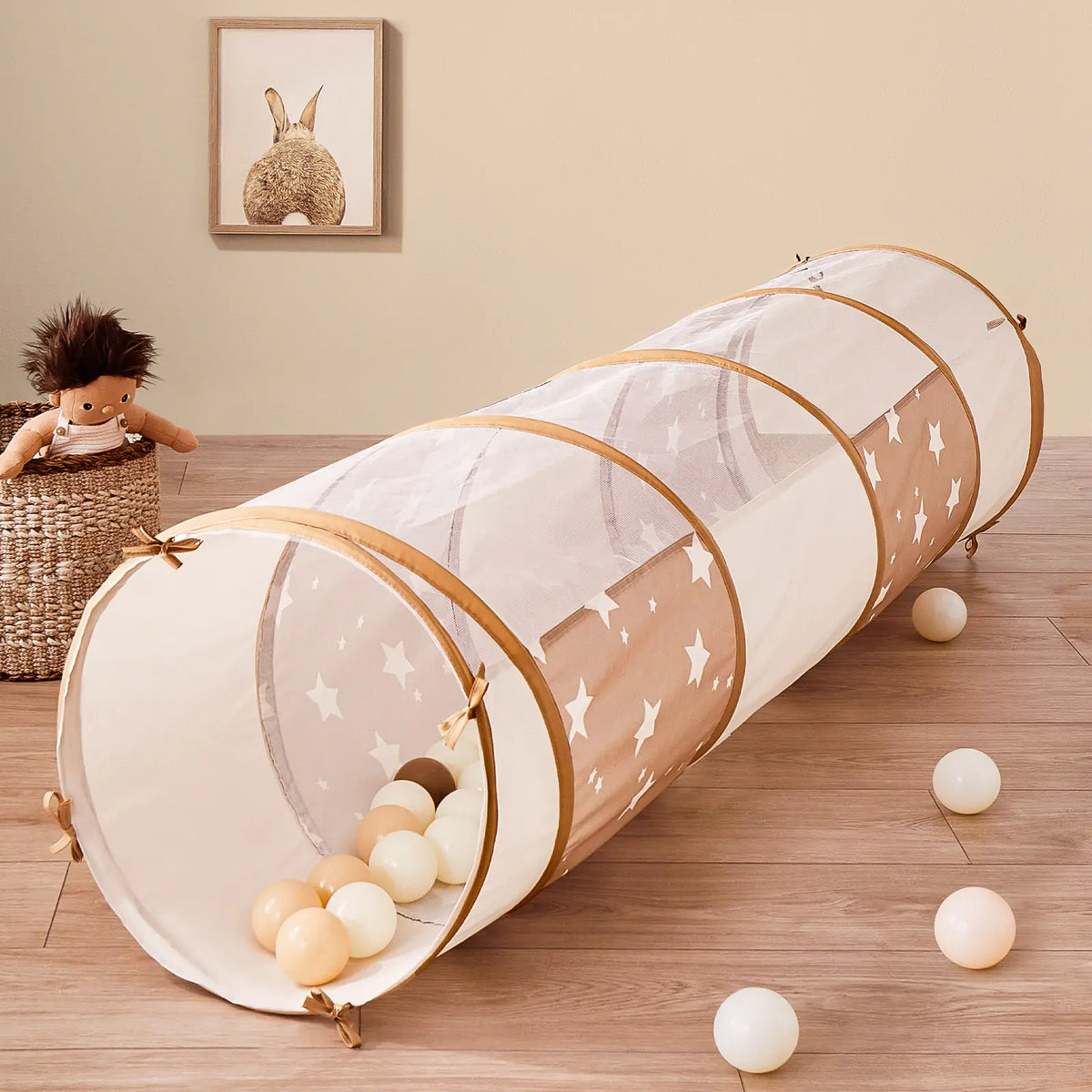 An Adventure Crawl Tunnel (68″) in brown and white, featuring a star pattern, a cylindrical shape, and plastic balls inside and scattered on the floor.