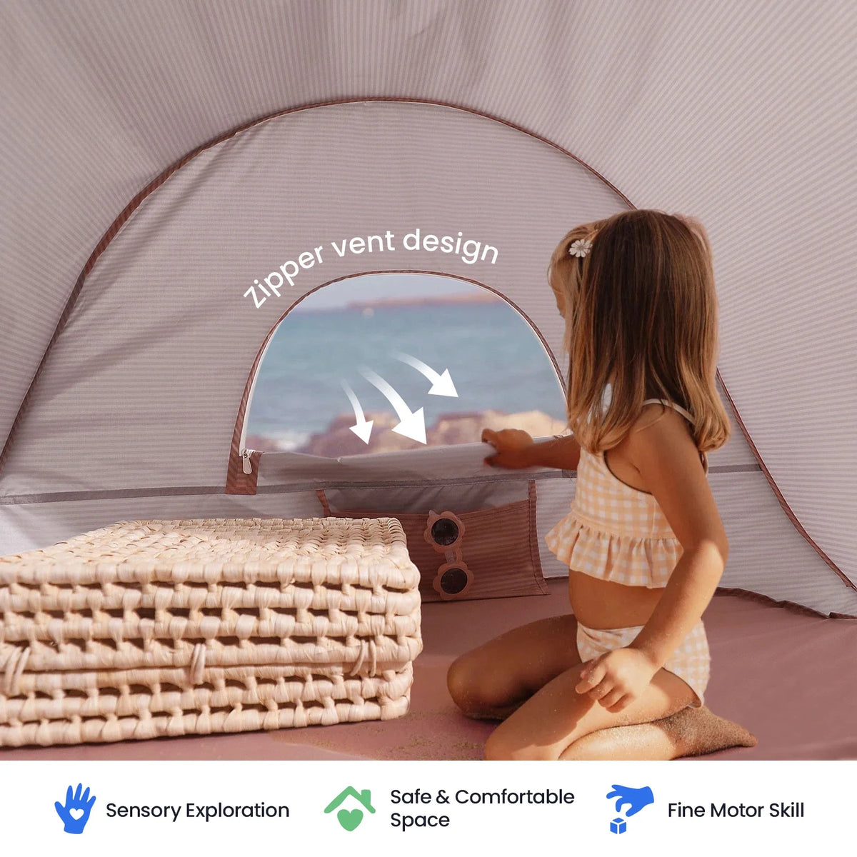 A child sits inside a Kids Beach Tent & Sand Toy Set, opening a zippered window that looks out toward the ocean, with icons below highlighting sensory exploration, a safe space, and fine motor skills.
