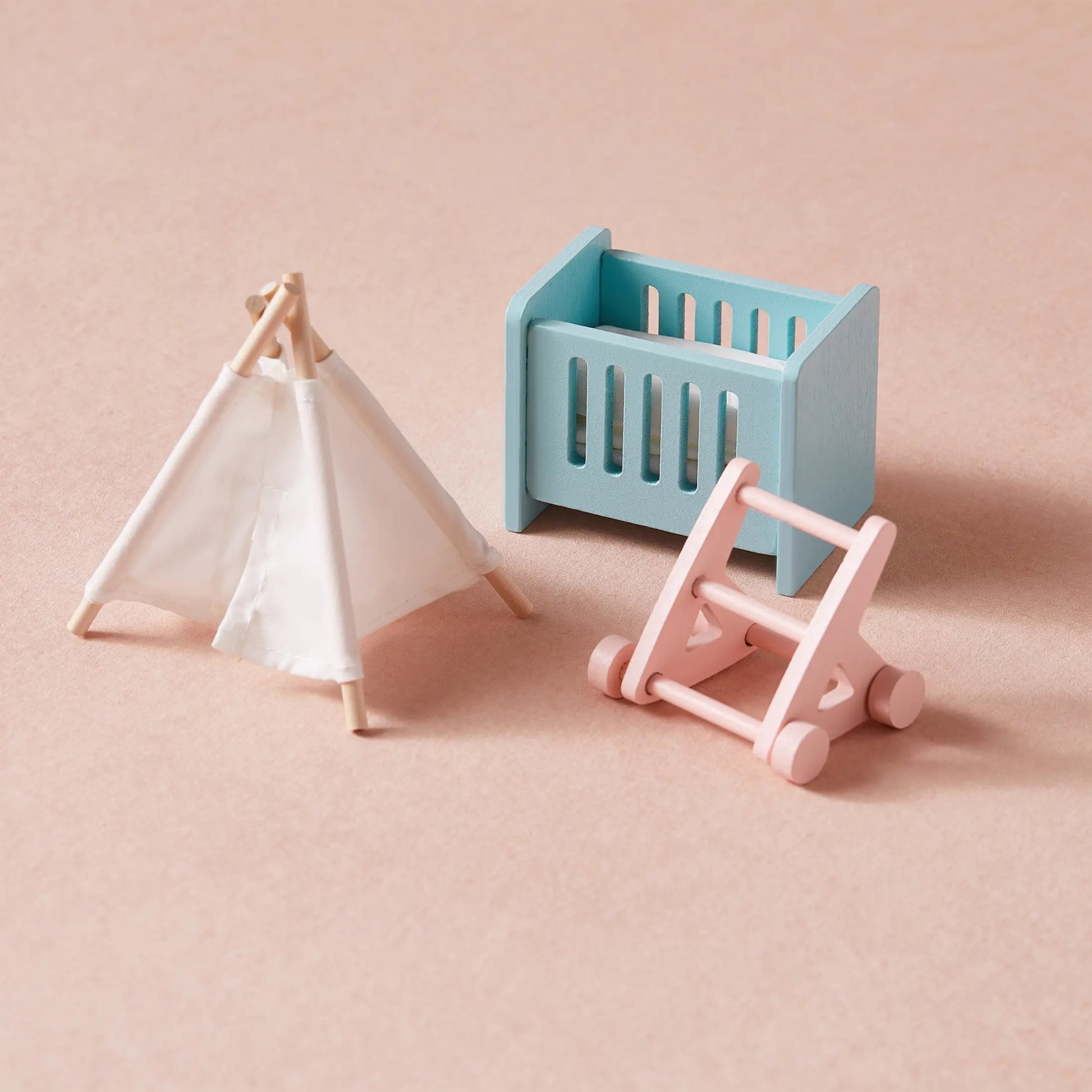 Three classic toys—a white teepee tent, a blue crib, and a pink baby walker—sit on a light peach background, perfect for imaginative play in the Tiny Land® Sweetwood Love Dollhouse without Dolls.