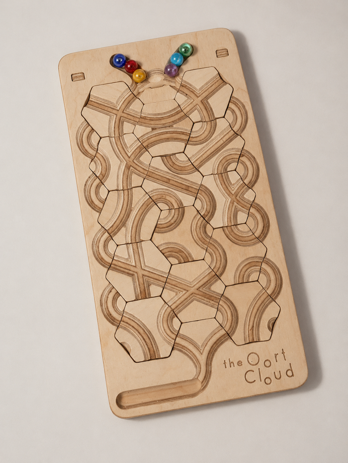 The Oort Cloud – Wooden Marble Run Puzzle featuring interlocking hexagonal tiles with carved tracks and colorful glass marbles resting at the top.
