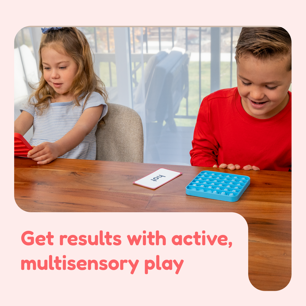 A girl and a boy sit at a table using Word Pop! + Extra CVC Mats, utilizing letter-themed sensory pop-it toys and a word card for blending letter sounds.
