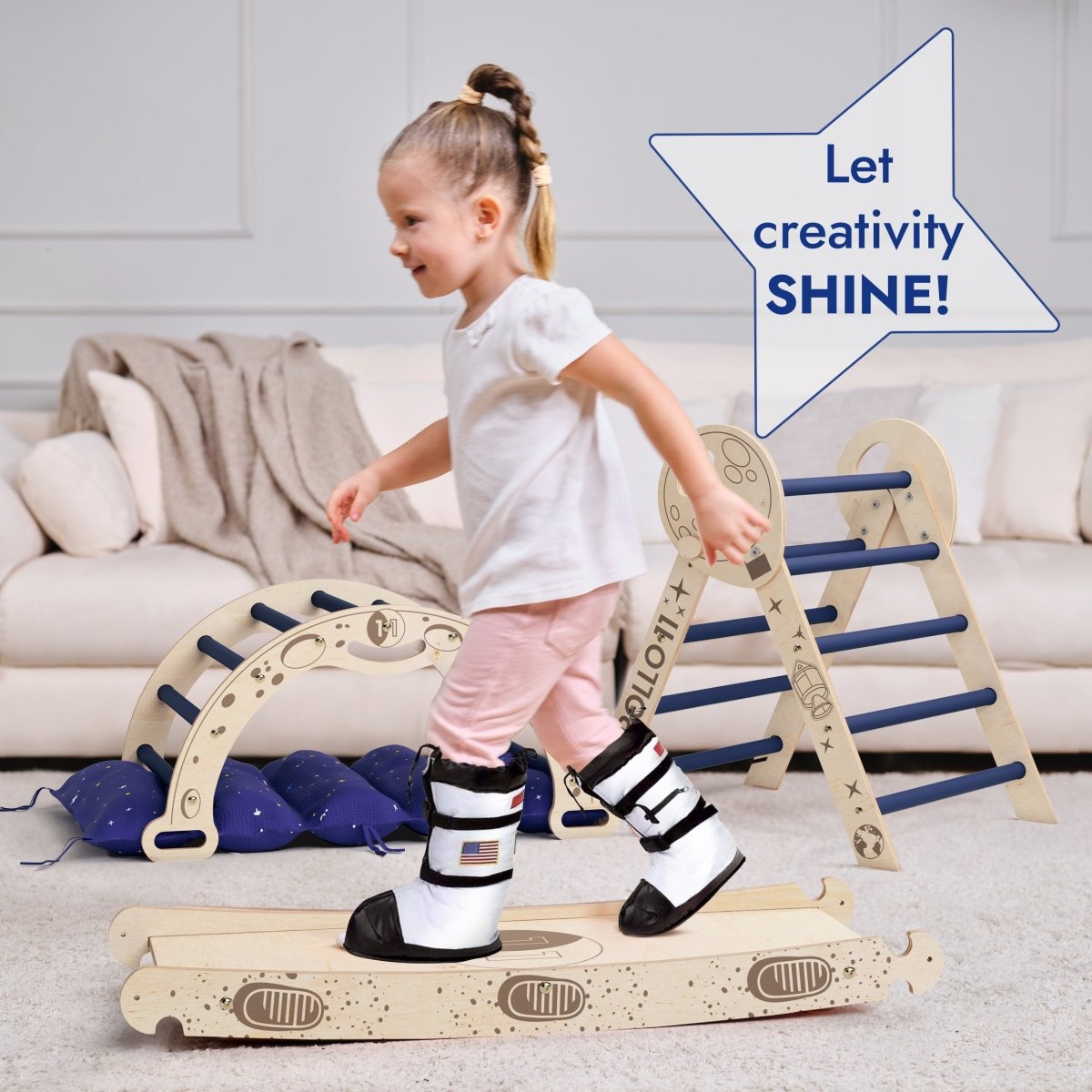 A young girl in space boots walks across a wooden balance board in a playroom filled with toddler climbing toys, including the Apollo 4in1 Climbing Set: Pikler Triangle, Arch, Slide Board, and Cushion for Little Toddlers Astronauts (1–3 Years). A speech bubble says, Let creativity SHINE!.