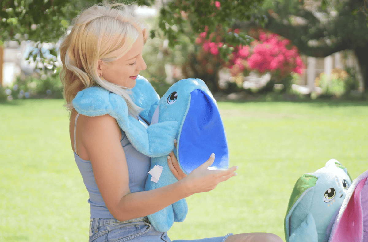 A woman holds a Bo the Moon Pal – 5 lb Weighted Plush, an ultra-soft, jumbo weighted toy with large ears and cartoonish eyes.