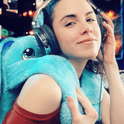 A person wearing headphones with a Bo the Moon Pal – 5 lb Weighted Plush, an ultra-soft blue plush rabbit, draped over their shoulder.
