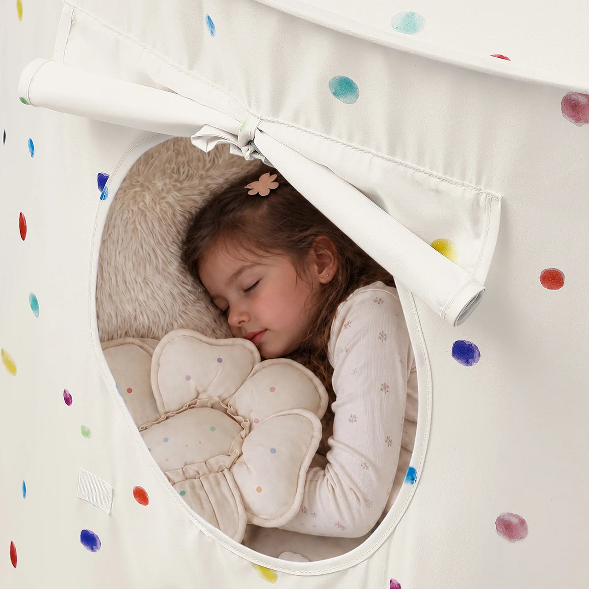 A young child sleeps inside a white polka-dot Starry Indoor Play Tent for Toddlers, resting on a flower-shaped pillow.