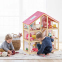 Two young children engage in imaginative play with the Tiny Land® Sweetwood Love Dollhouse without Dolls, decorated in pastel colors on a rug in a bright, cheerful room. A basket of plush toys sits nearby.