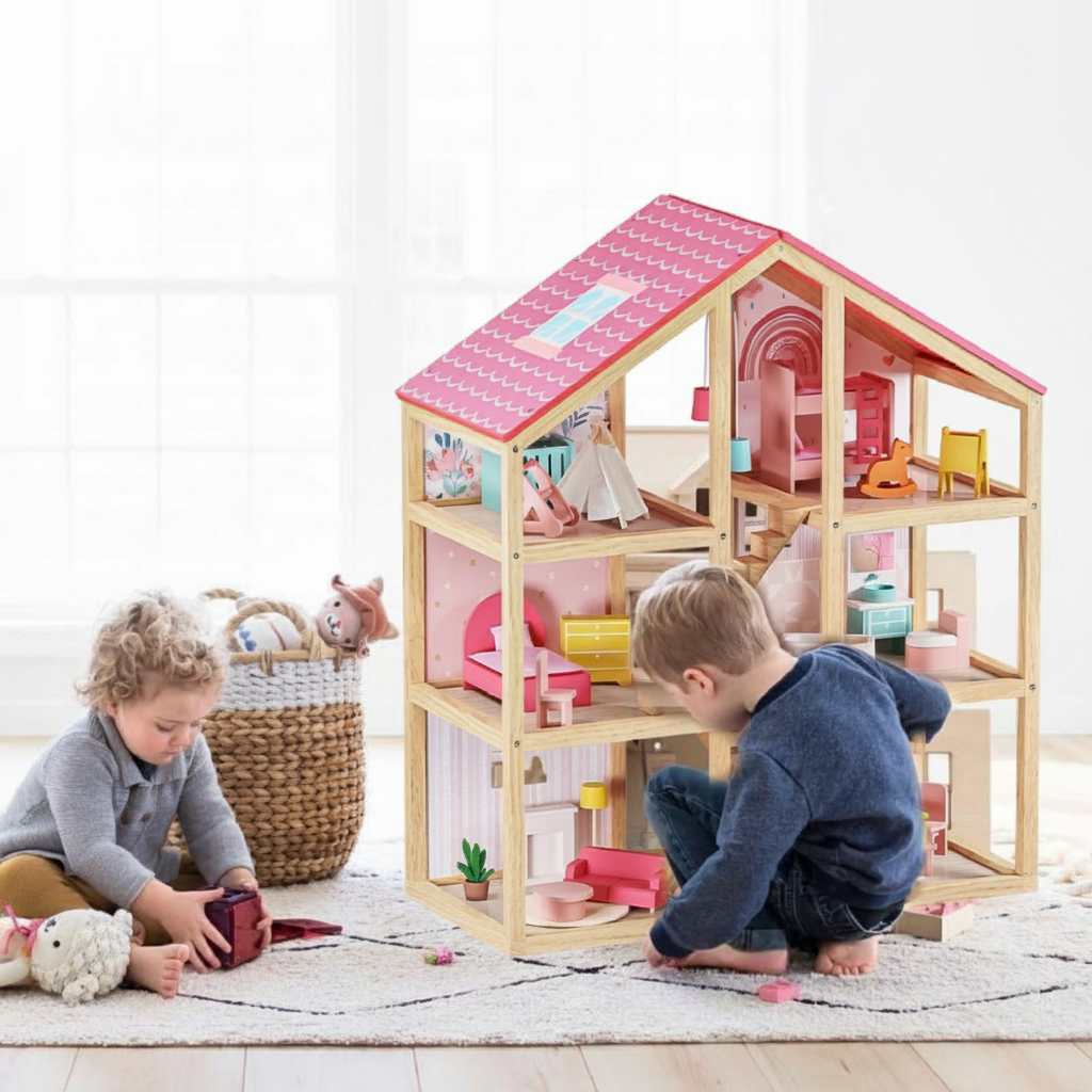 Two young children engage in imaginative play with the Tiny Land® Sweetwood Love Dollhouse without Dolls, decorated in pastel colors on a rug in a bright, cheerful room. A basket of plush toys sits nearby.