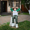 A young boy in green pants and a white-green shirt climbs the Climbing rope ladder for kids 3-9 y.o., attached to a tree in a backyard with grass, pavement, and a wooden house in the background, promoting muscle strengthening and supporting healthy child development.