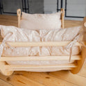 A small wooden cradle with beige polka-dot bedding and pillows tied with ribbons sits on a light wooden floor in a cozy room, perfectly complemented by our Cushion for Climbing Arch & Rocker Balance (Cushion Only) to enhance your little one’s comfort.