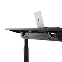 The Under Desk Cable Management Tray is shown beneath a sleek black standing desk with a laptop, demonstrating its adjustable height functionality and streamlined cable organization against a plain white background.