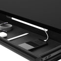 The Under Desk Drawer includes a coiled USB cable, a white stylus, a smartphone charging via USB, and a small white object, all organized for efficient under-desk storage.