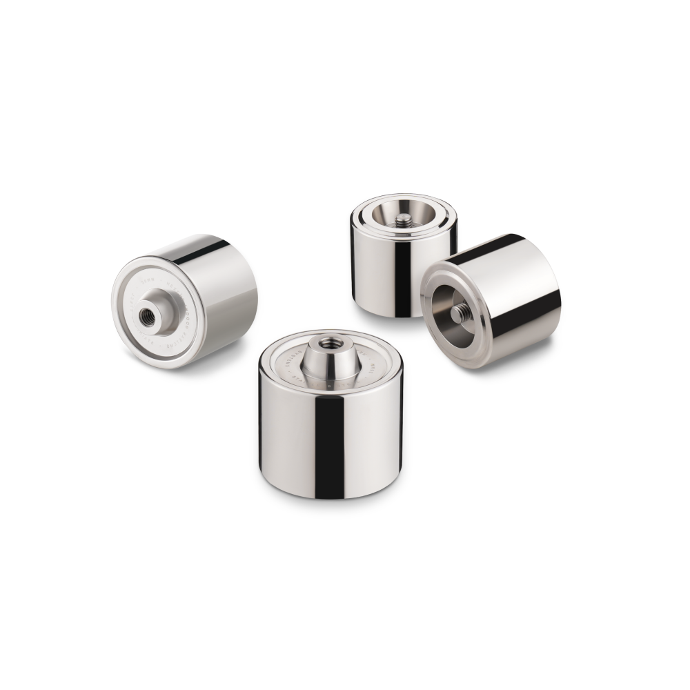 Four shiny, cylindrical metal components with central threaded holes from the Hexcal Studio Extension Kit are arranged on a white background—perfect for enhancing monitor positioning in an ergonomic desk setup.