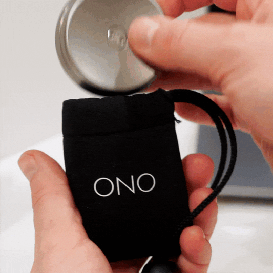 A person puts an ONO Slider Titanium fidget toy into a small black pouch labeled ONO in white letters and secures it with the drawstring.
