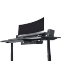 The Hexcal Elevate Standing Desk in black features height adjustability, a large curved monitor, two speakers, and a keyboard tray, all set against a plain white background.