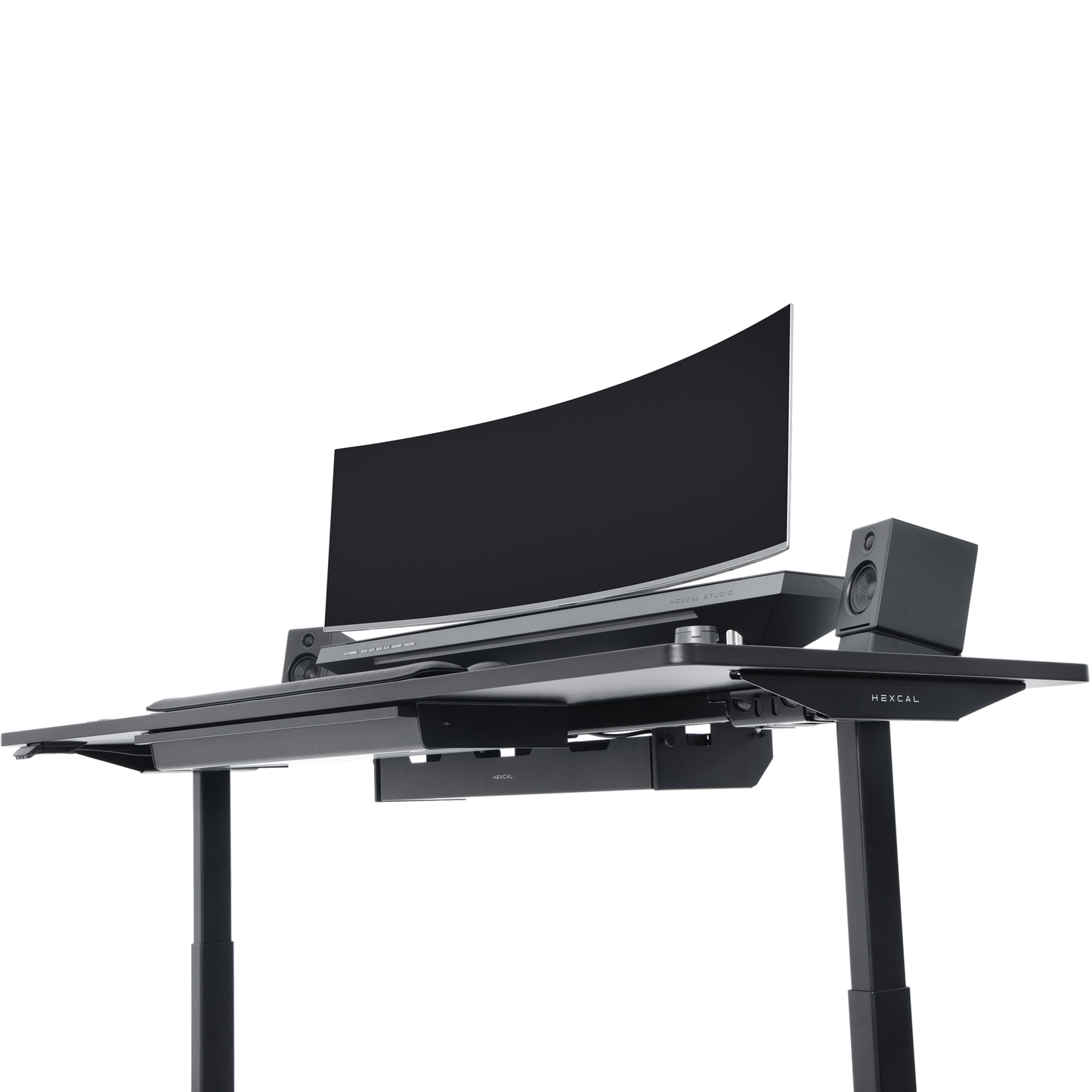 The Hexcal Elevate Standing Desk in black features height adjustability, a large curved monitor, two speakers, and a keyboard tray, all set against a plain white background.