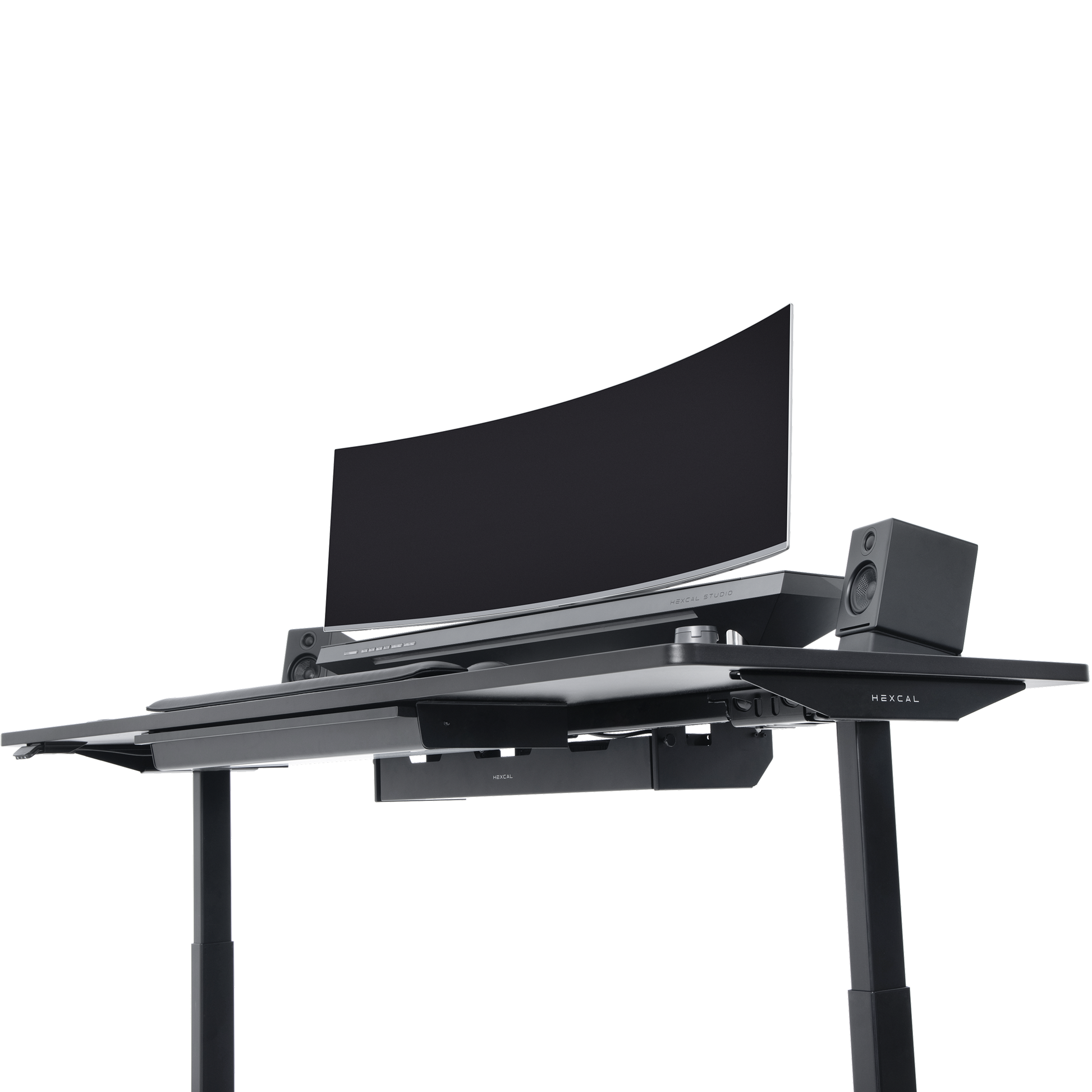 The Hexcal Elevate Standing Desk in black features height adjustability, a large curved monitor, two speakers, and a keyboard tray, all set against a plain white background.