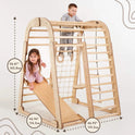 Two young children play on the Indoor Wooden Playground for Children - 6in1 Playground + Swings Set + Slide Board, a Montessori-inspired wooden climbing structure with a slide. This kids playground features clearly marked dimensions—height: 56.61 in (143.8 cm), width: 44.96 in (114.2 cm), and length: 46.92 in (119.2 cm)—making it an ideal indoor playset for active little ones.