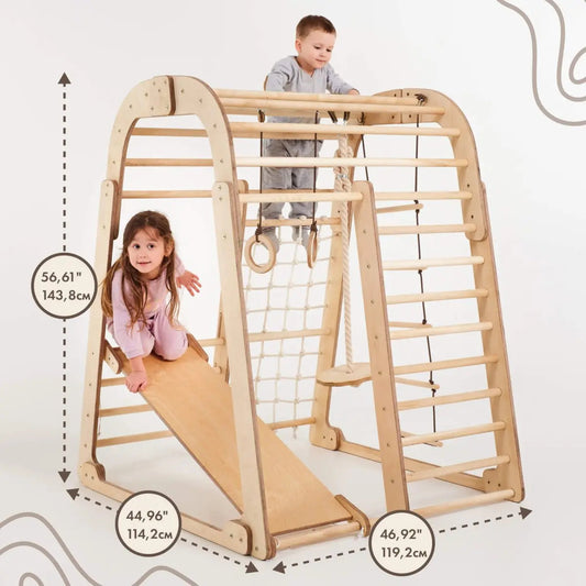 Two young children play on the Indoor Wooden Playground for Children - 6in1 Playground + Swings Set + Slide Board, a Montessori-inspired wooden climbing structure with a slide. This kids playground features clearly marked dimensions—height: 56.61 in (143.8 cm), width: 44.96 in (114.2 cm), and length: 46.92 in (119.2 cm)—making it an ideal indoor playset for active little ones.