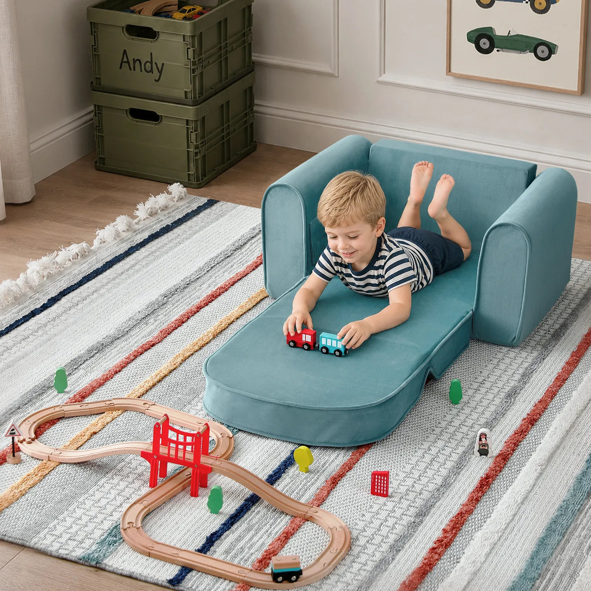 A young boy lies on his stomach on a teal blue GentleSnug Flip-Open Kids Sofa & Nap Mat, playing with small wooden toy trains on a track on the floor.