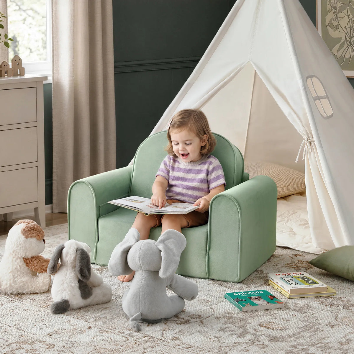 A young child sits in a pale green GentleSnug Flip-Open Kids Sofa & Nap Mat, reading a book while surrounded by stuffed animals and a play tent.
